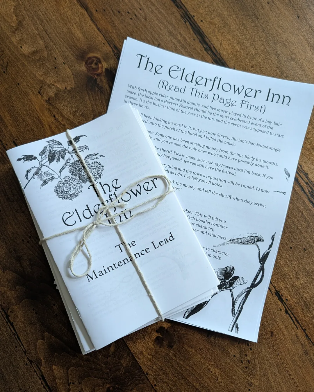 Playtest booklets, bound in string, on top of the one-page instructions for The Elderflower Inn parlor larp.