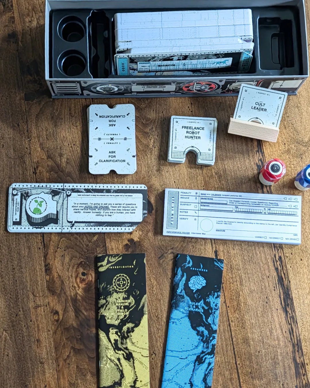 The contents of the social deduction game, Inhuman Conditions, including sheets, booklets, and stamps.