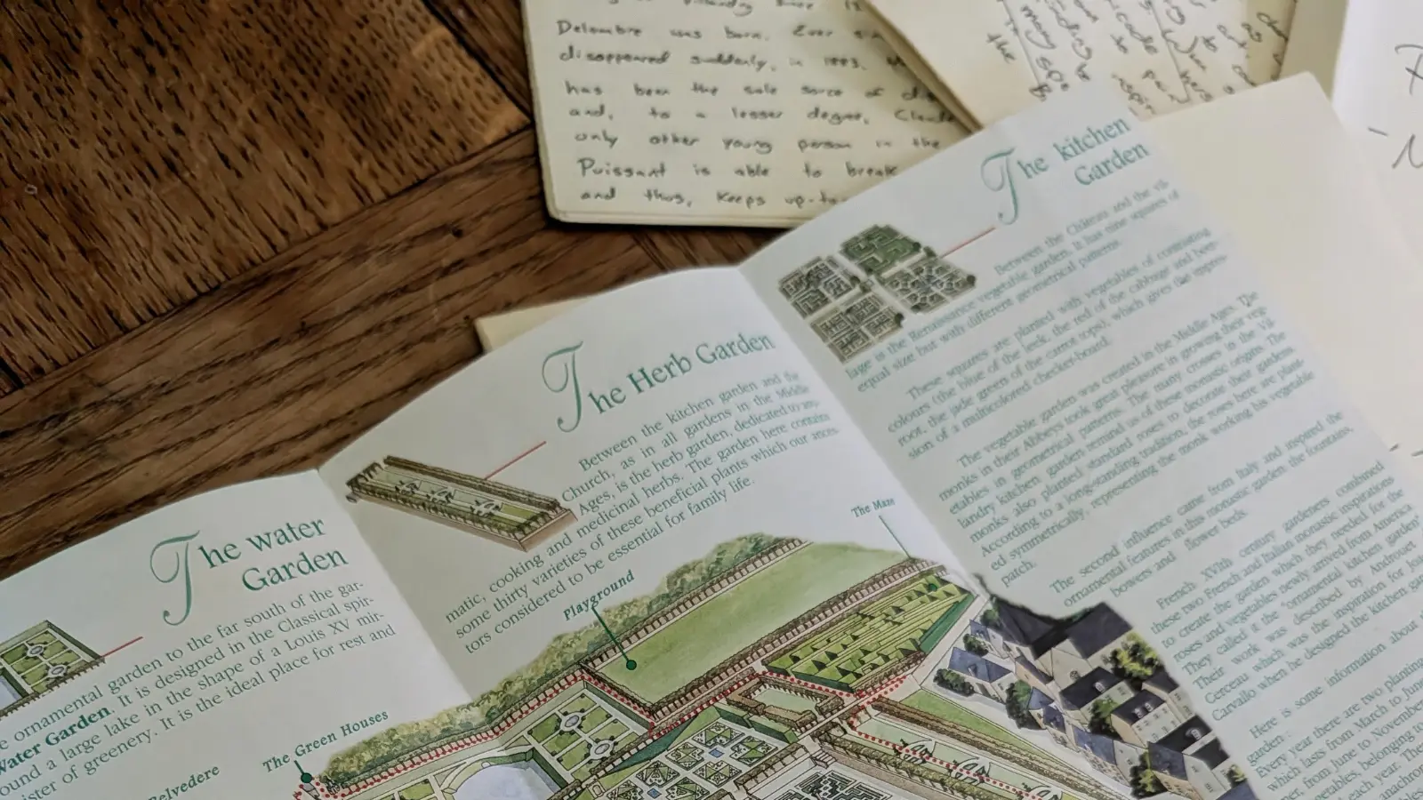 A fold-out Château de Villandry visitor brochure showing illustrated maps of the water garden, herb garden, and kitchen garden, open beside handwritten character pages.